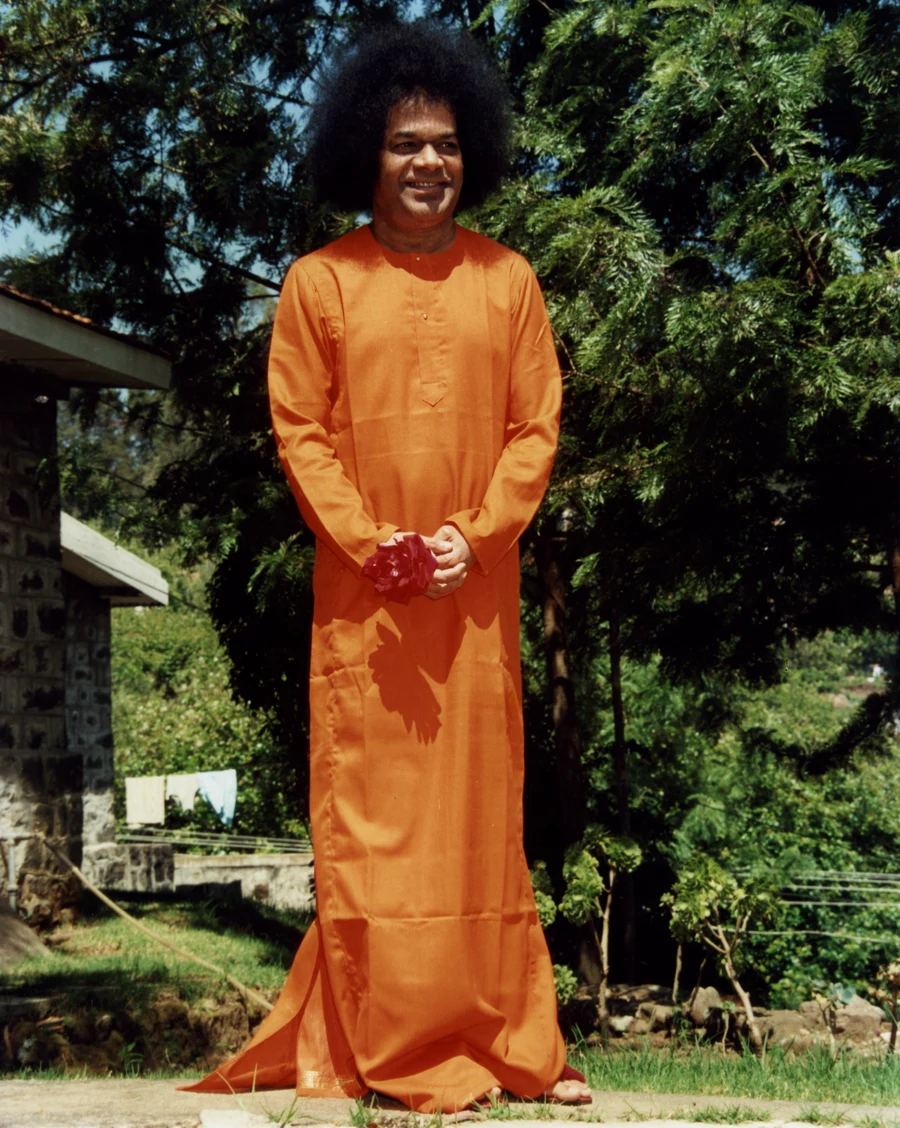 Bhagavan Sri Sathya Sai Baba standing outdoors with flowers